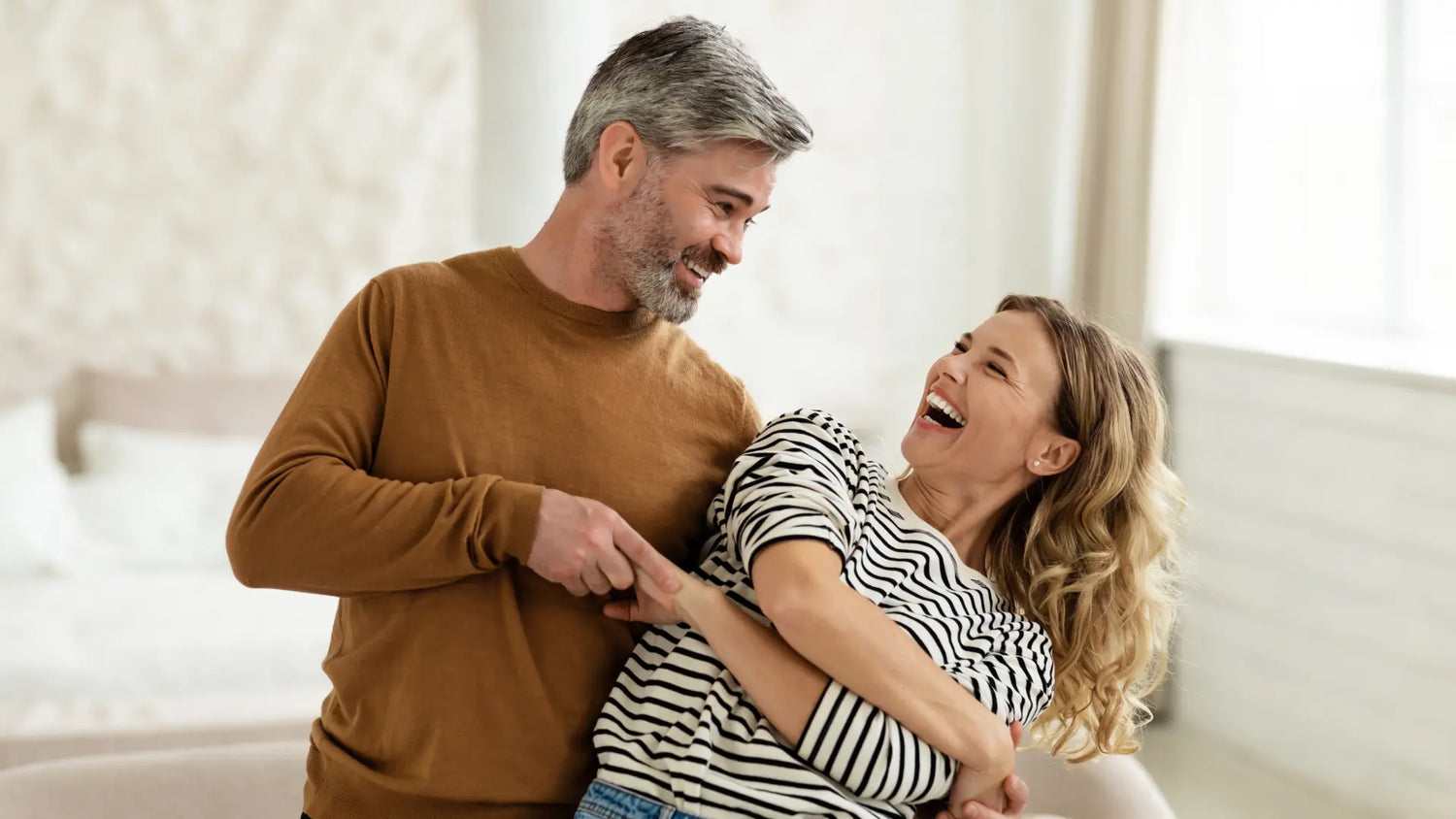 Coppia sorridente che gioca insieme in un ambiente domestico, simbolo di vitalità e benessere.
