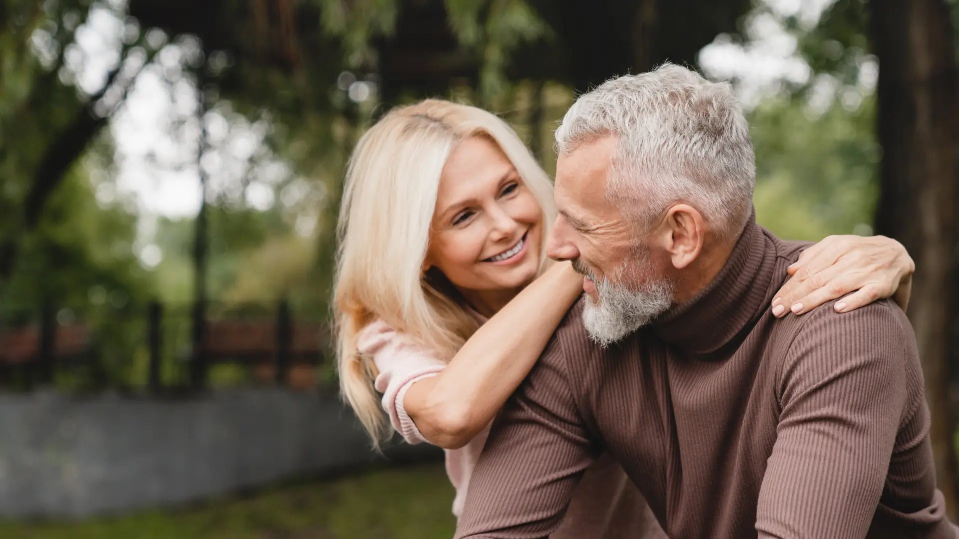 Coppia matura che sorride e si abbraccia all'aperto, in un contesto naturale e sereno