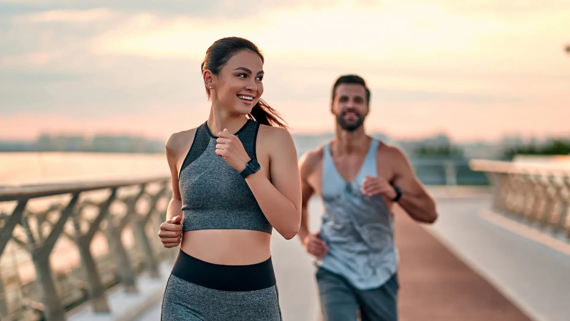 Donna e uomo che corrono all'aperto su una passerella al tramonto.