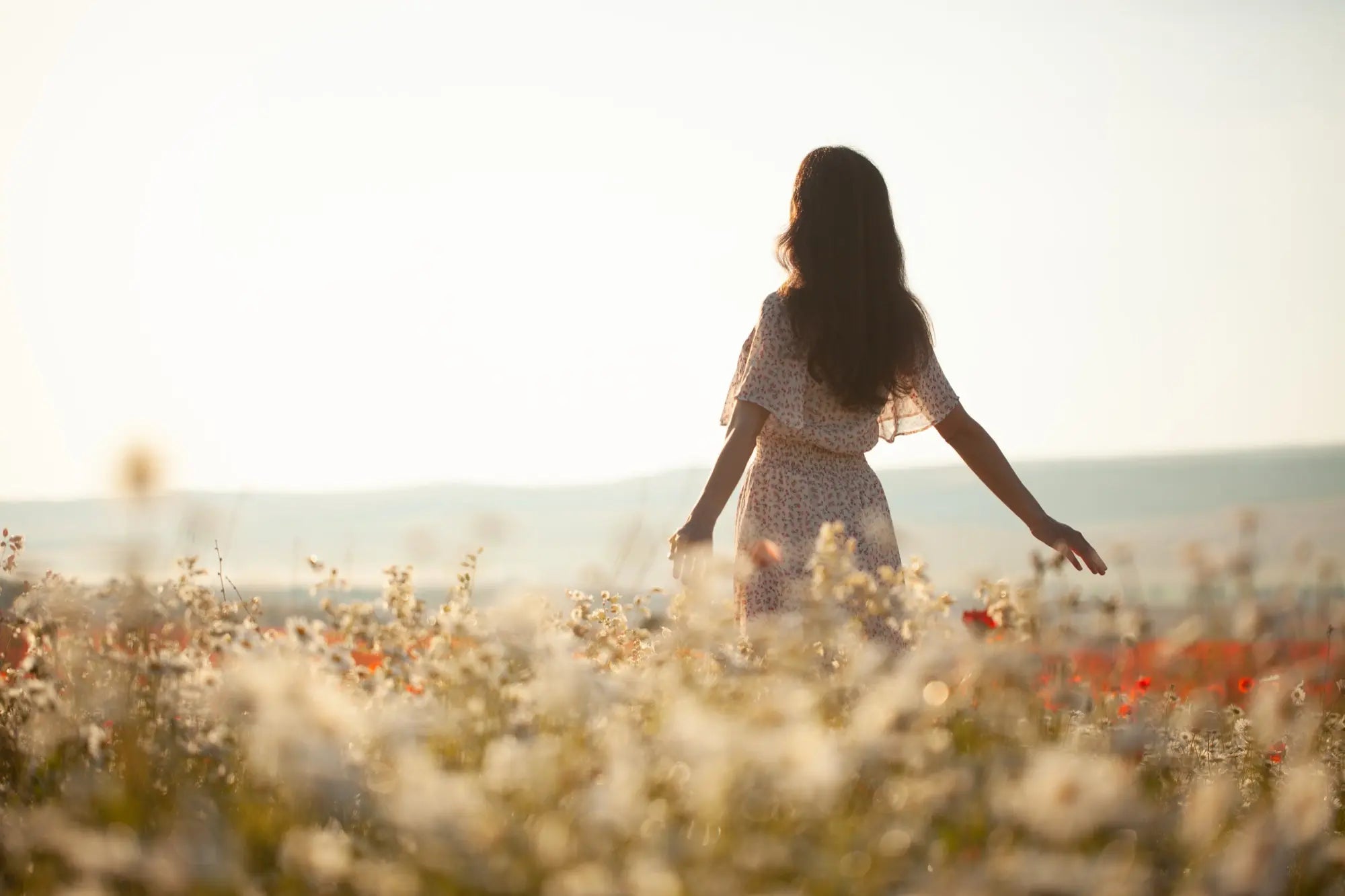 Donna che cammina tra i fiori in un paesaggio naturale, in un momento di pace e libertà.