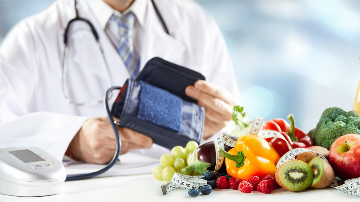 Medico che misura la pressione con uno sfigmomanometro, accanto a frutta e verdura fresca e un metro da sarta, simboli di uno stile di vita sano