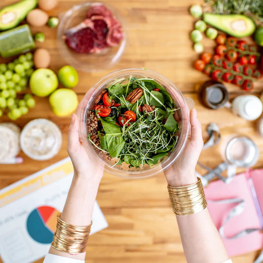 Vista dall’alto di una persona che tiene una ciotola con insalata fresca, circondata da alimenti sani e ingredienti naturali su un tavolo
