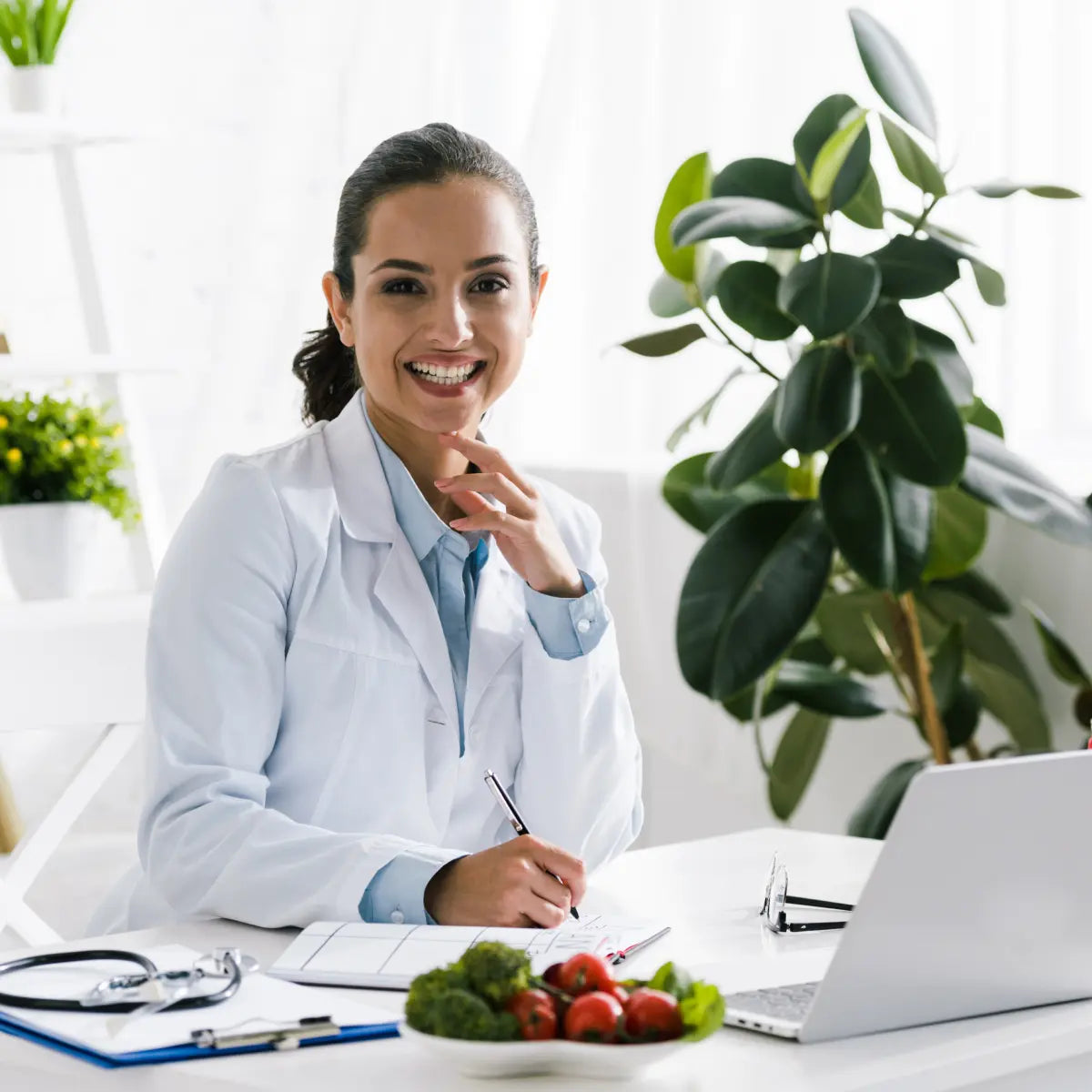 Dottoressa sorridente alla scrivania con computer portatile, stetoscopio e piatto di verdure