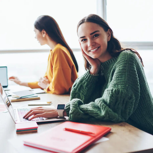 Studentessa sorridente seduta alla scrivania con computer portatile e quaderni