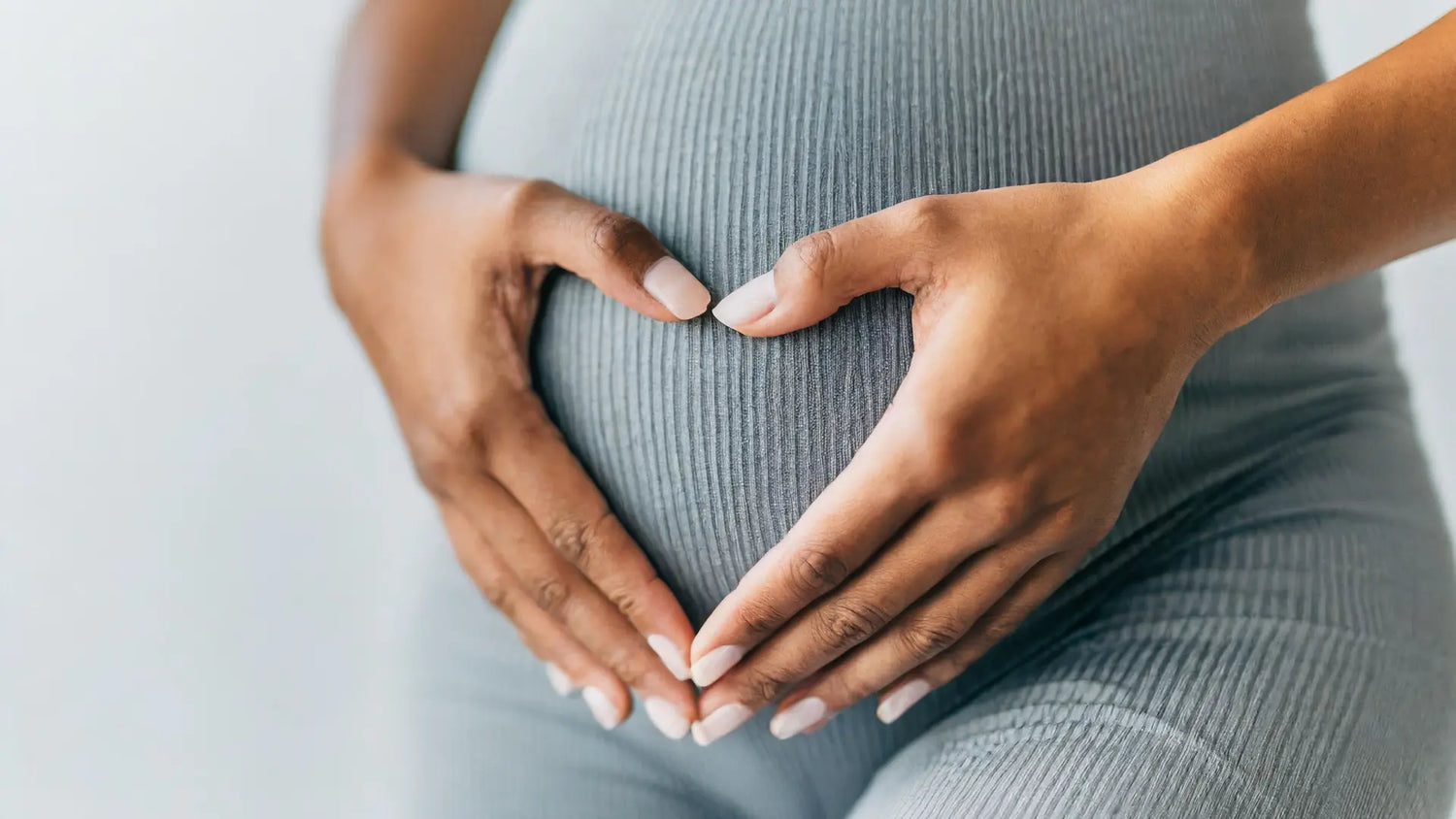 Donna incinta che forma un cuore con le mani sul pancione, simbolo di amore materno e gravidanza